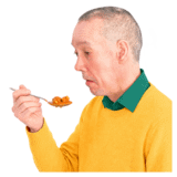 A man in a yellow top eating food with a spoon.
